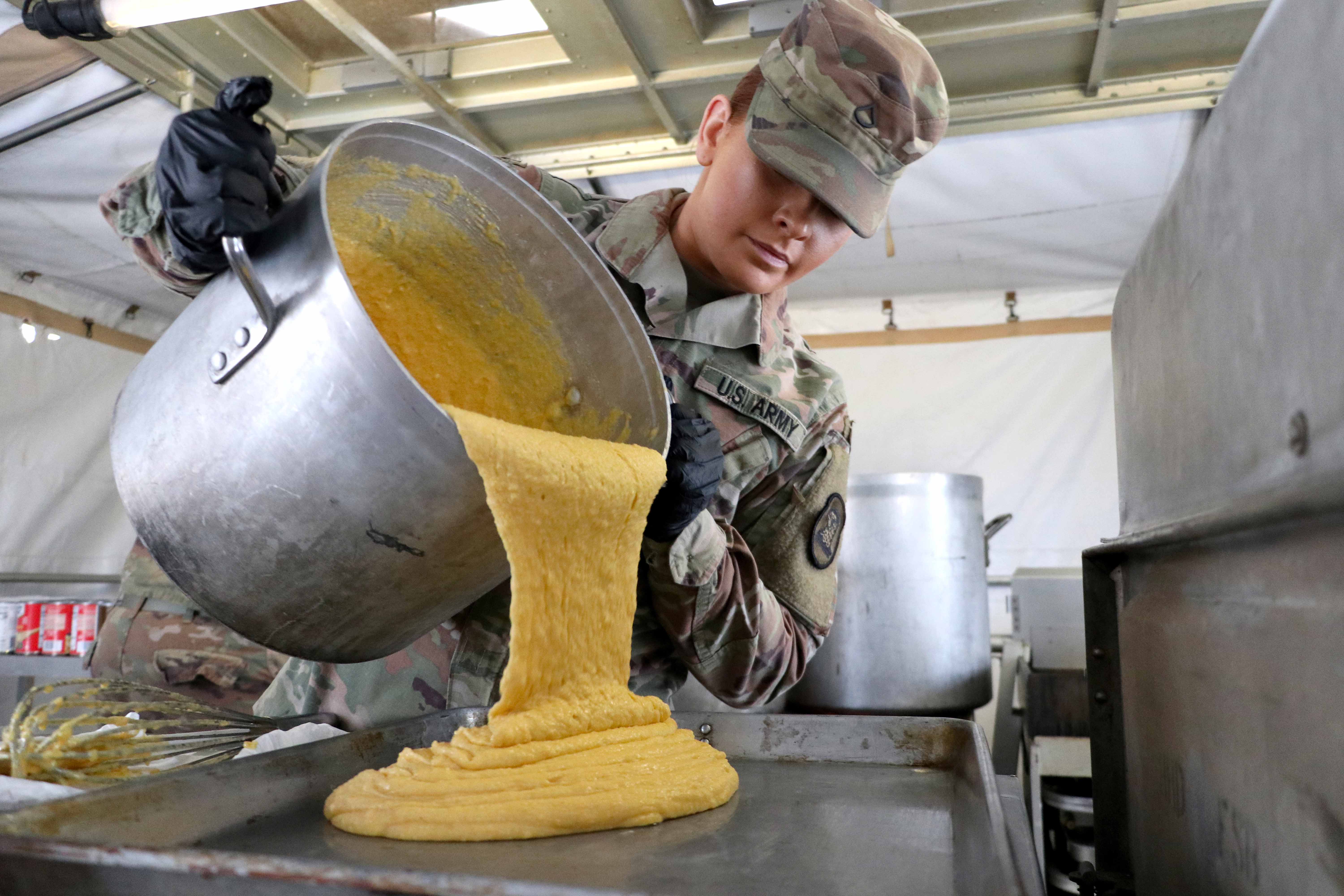 Military chef pouring food from a large vessel