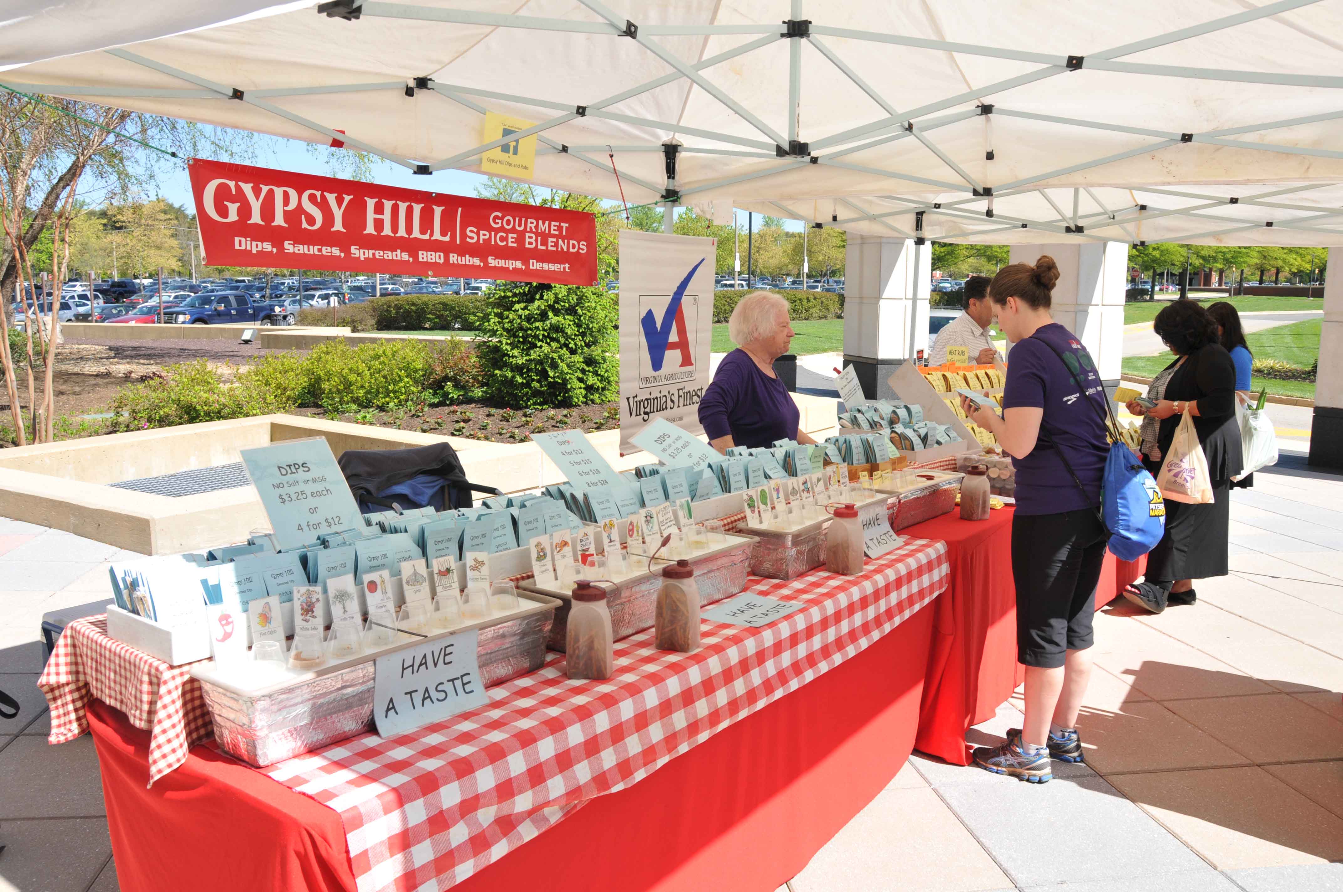 Beneath a white canopy tent is a red checkered table lined with different types of dips and rubs.  There is a red sign above the table, labeled “Gypsy Hill