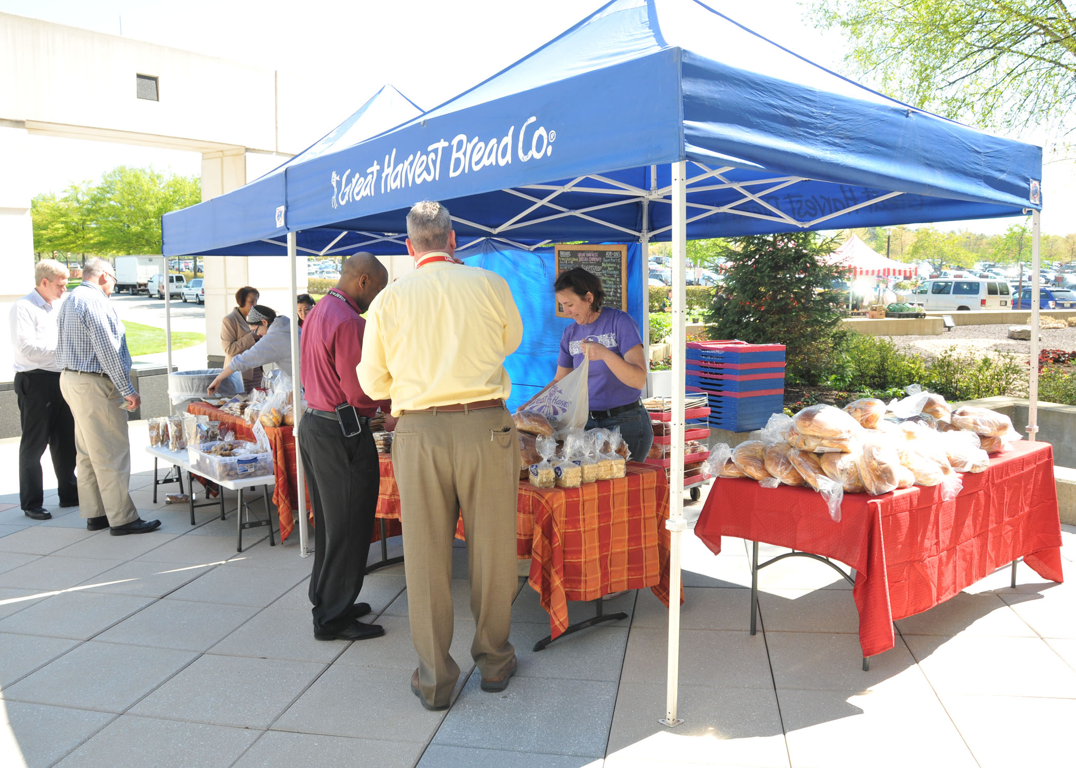 A blue canopy tent with the words Great Harvest Bread Co stands over tables covered in different types of bread