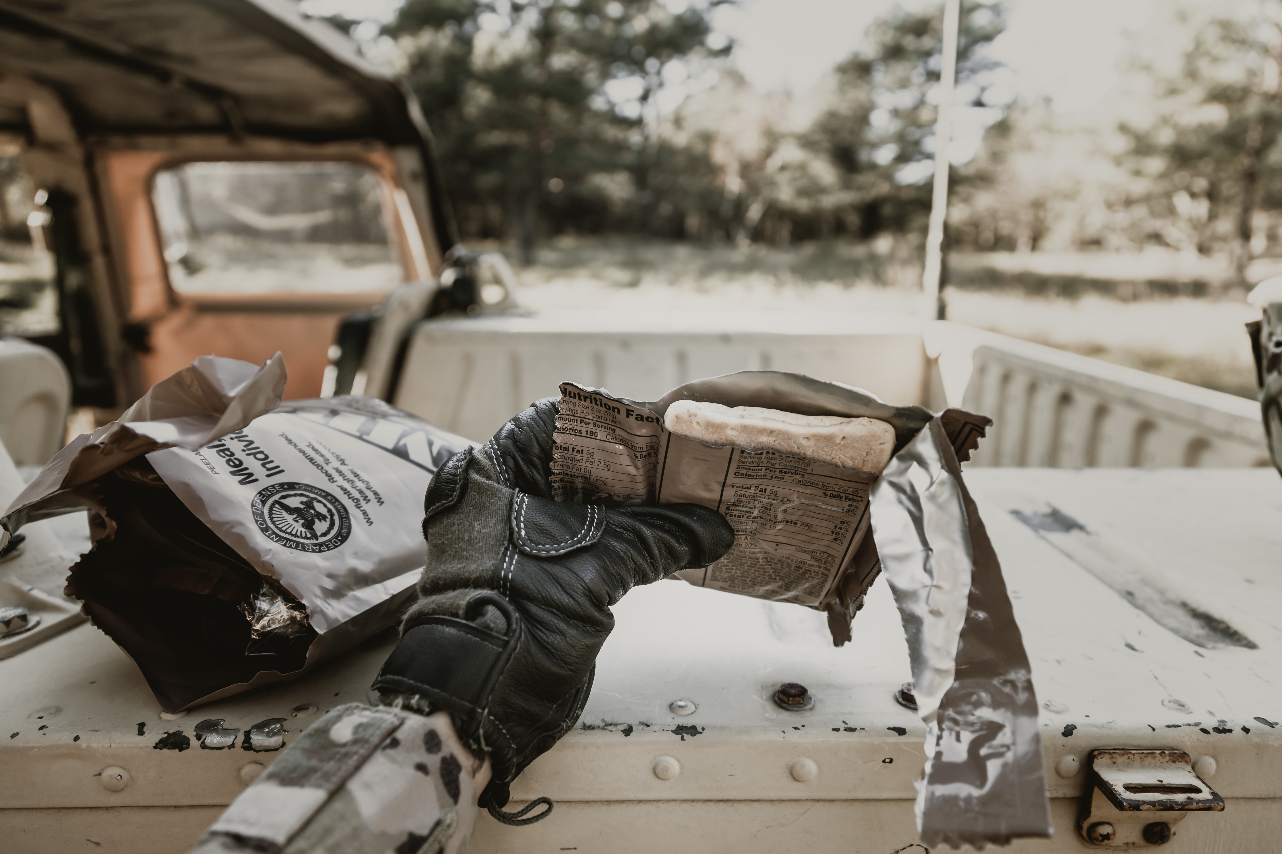 A gloved hand holds an opened pack from an MRE outdoors A gloved hand holds an opened pack from an MRE outdoors