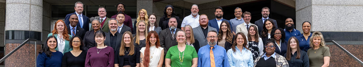 A group of DLA employees consisting of men and women standing in formal attire in front of a building.