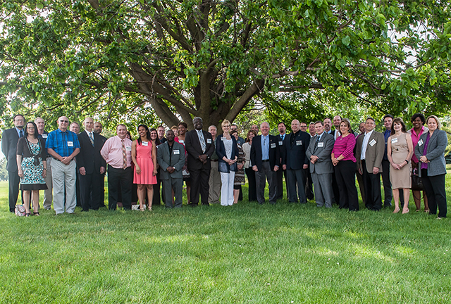 Former level three participants gather underneath a large tree in a grassy field. 
